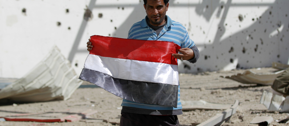 A Yemeni man poses with a national flag at a sports hall that was partially destroyed by Saudi-led air strikes in the Yemeni capital Sanaa on January 19, 2016. / AFP / MOHAMMED HUWAIS