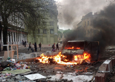 Voiture en flammes dans une rue dévastée.